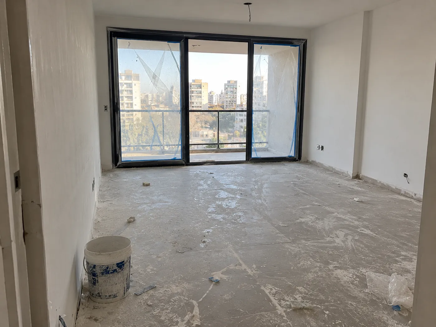 Living de departamento a estrenar antes de la limpieza, con restos de pintura y pastina en el piso y cinta en las aberturas