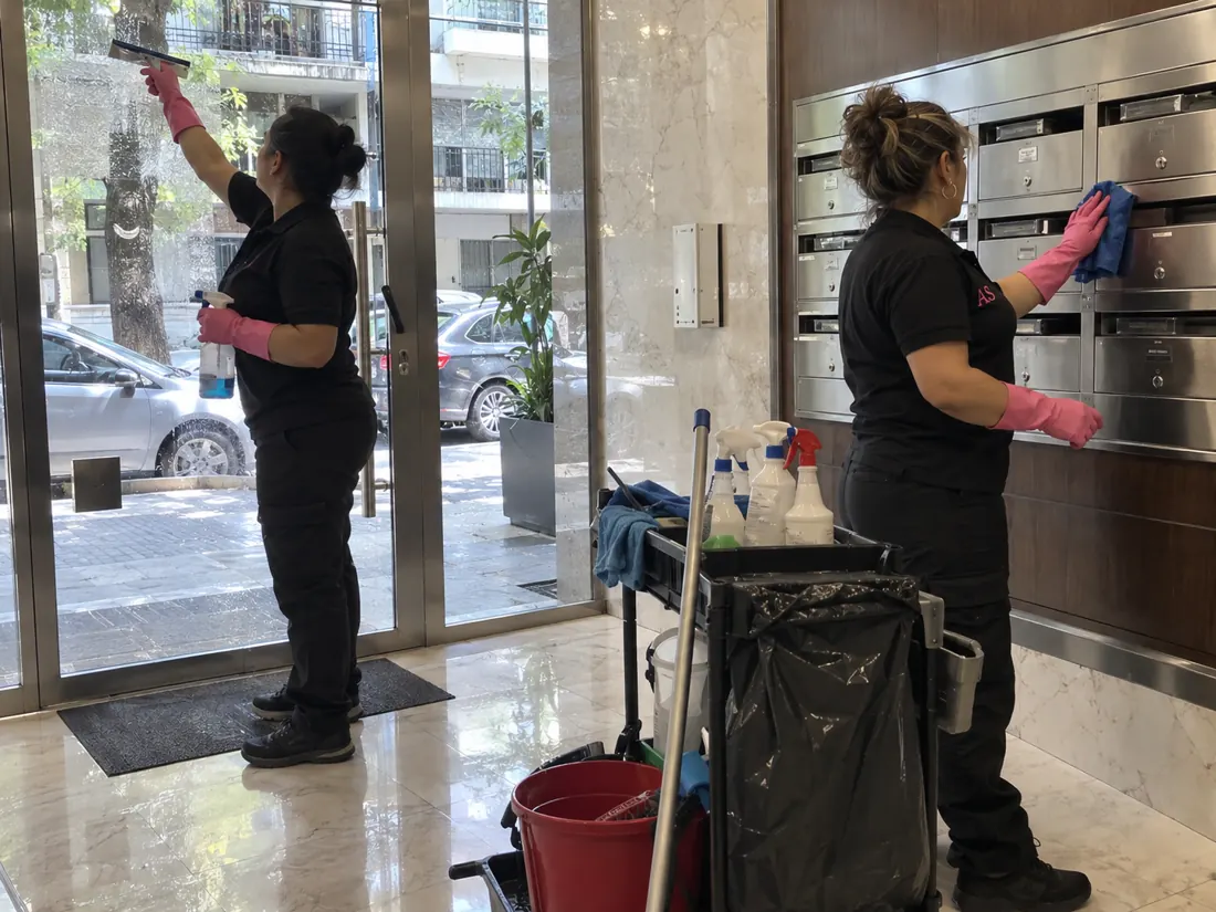 Dos operarias de Aqua Simplicity limpiando la puerta de vidrio y los buzones del hall de un edificio sin encargado