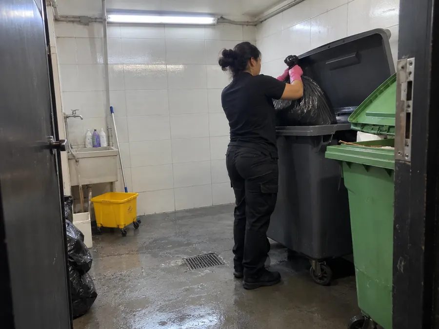 Operaria retirando las bolsas de residuos al contenedor en la sala de residuos del edificio